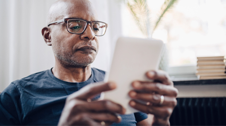 Retired senior man reading e-book in room at home