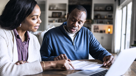 Husband and wife looking over bills and using laptop in domestic kitchen